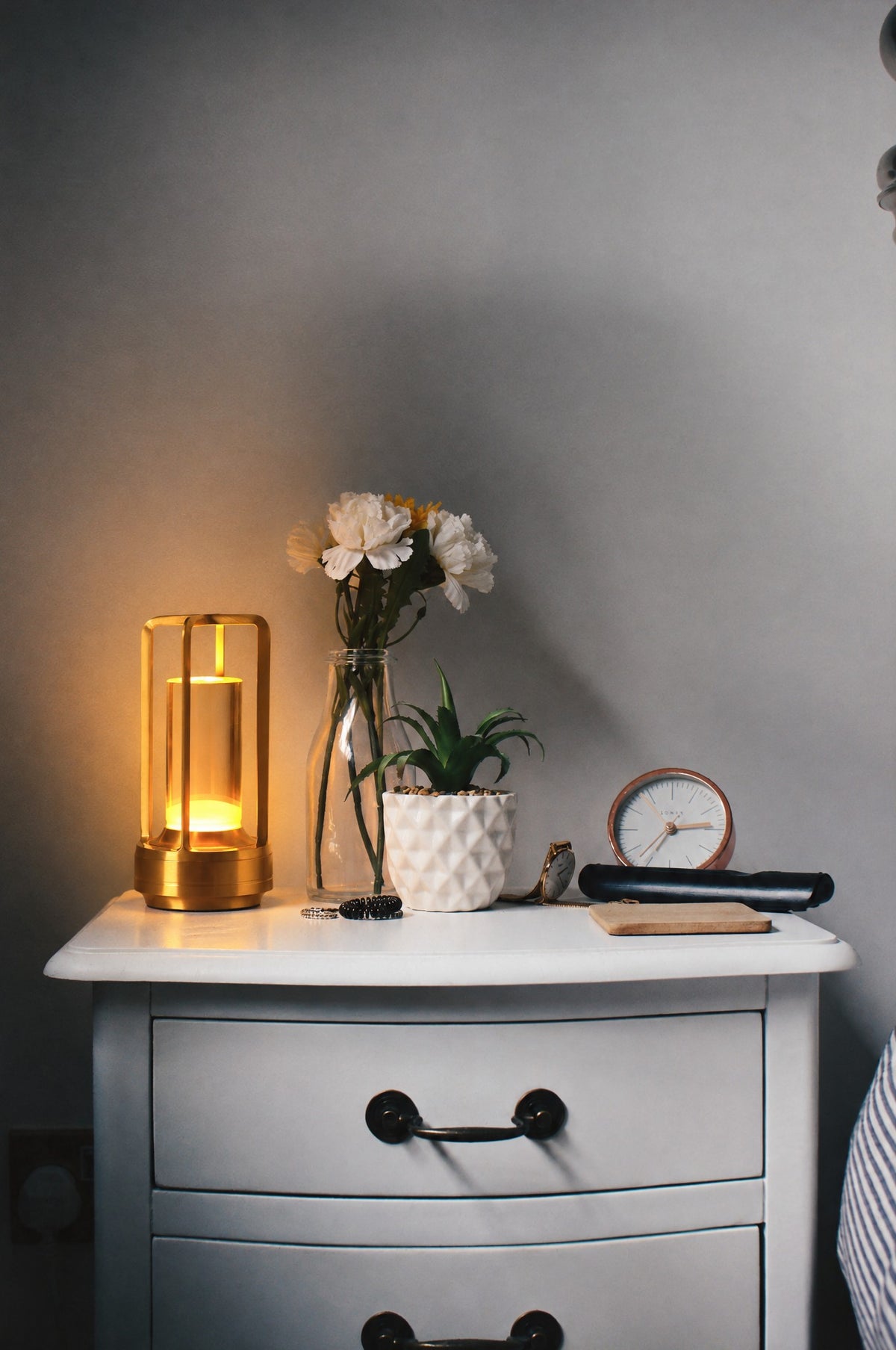 Gold cordless lantern table lamp, 7 in tall, on a bedside nightstand next to a flower vase and clock, shown to scale